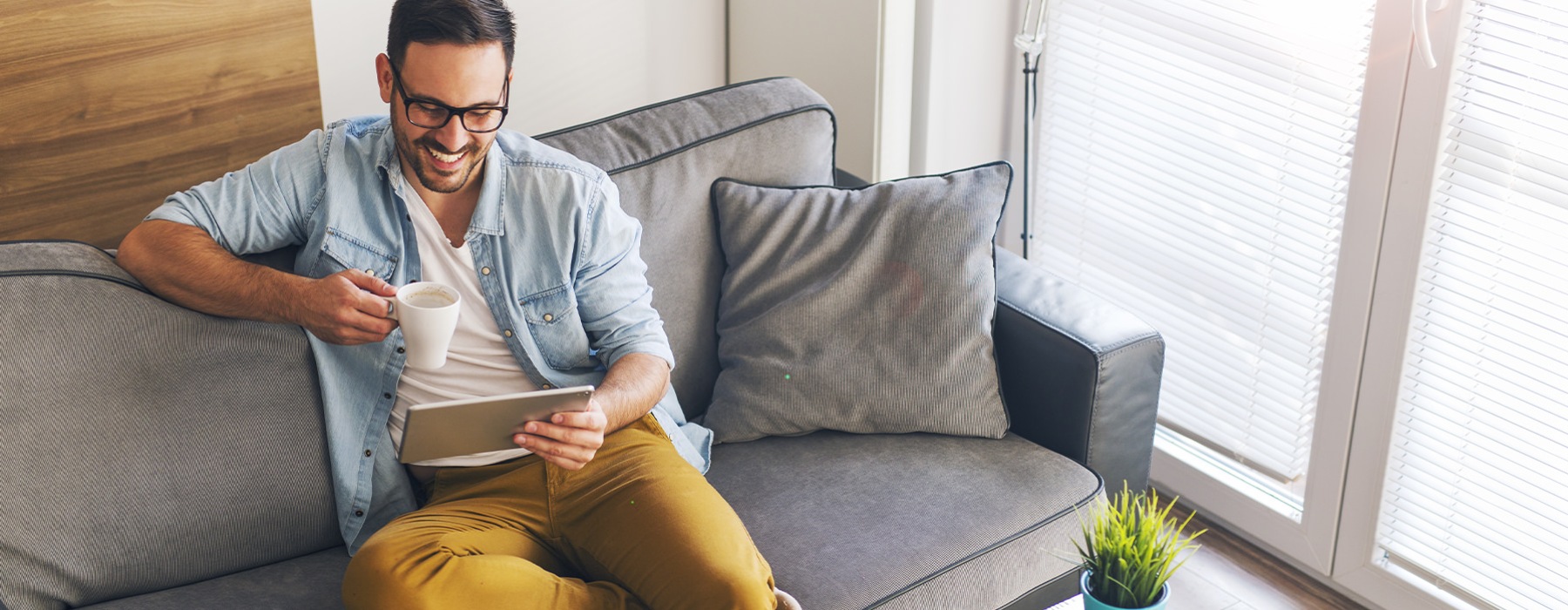 A resident sipping coffee and looking at an ipad at The District Apartments in Pittsburgh, PA, featuring natural lighting.